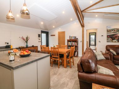 An open living and dining area with a kitchen island bowls of fruit wooden dining table brown leather sofas and bookshelves at Stables Lodge in Wingerworth