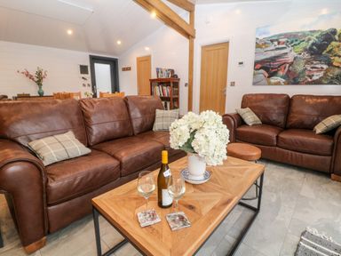 A living room with two brown leather sofas a wooden coffee table with flowers and wine at Stables Lodge in Wingerworth