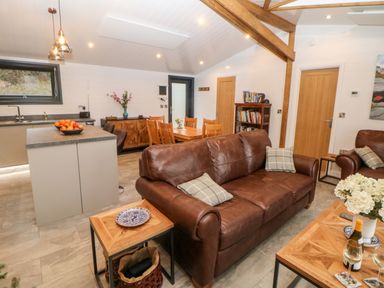 A living room with brown leather sofas wooden tables and a dining area with chairs and bookshelf at Stables Lodge in Wingerworth