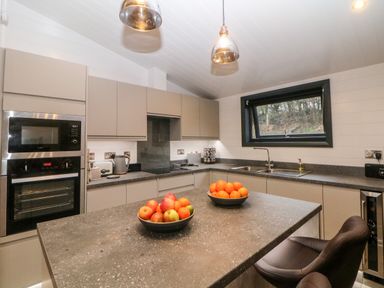 A modern kitchen with an island counter bowls of fruit oven microwave sink window and two pendant lights at Stables Lodge in Wingerworth