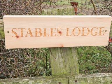 A wooden sign with the text Stables Lodge mounted on a weathered wooden post outdoors at Wingerworth