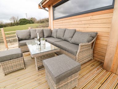 An outdoor seating area with a wicker sofa set and glass table on a wooden deck at Stables Lodge in Wingerworth