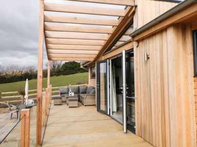 A wooden patio with outdoor seating and glass railing attached to a wooden building at Stables Lodge in Wingerworth
