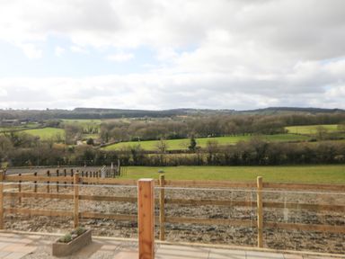 A rural outdoor scene with wooden fencing and fields with trees and hills in the background at Stables Lodge in Wingerworth