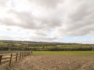 A fenced muddy field with green grass and distant hills under cloudy sky at Stables Lodge in Wingerworth