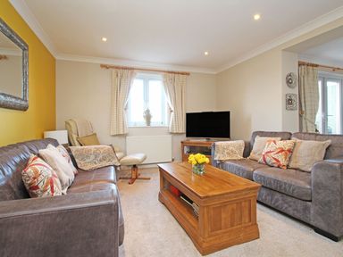 A living room with two sofas a wooden coffee table a lounge chair a television and window with curtains at Wheal Kendall in Mevagissey