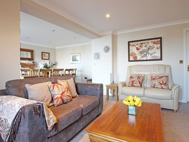A living room with two sofas a wooden coffee table with yellow flowers and a dining table with chairs at Wheal Kendall in Mevagissey