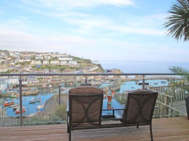 A balcony with two chairs and a table overlooking a harbor with boats and houses at Wheal Kendall in Mevagissey