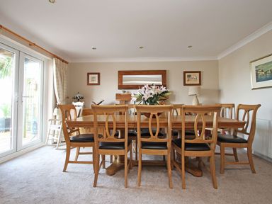 A dining room with a wooden table and chairs a vase with flowers a mirror and framed pictures at Wheal Kendall in Mevagissey