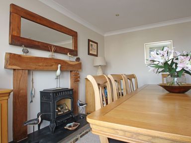 A dining room with a wooden table and chairs a floral arrangement on the table a wood stove with decorative birds and a wooden mantle with a large mirror on the wall at Wheal Kendall in Mevagissey