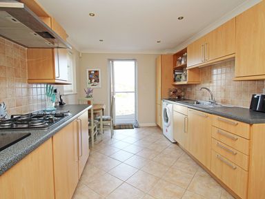 A kitchen with wooden cabinets a gas stove a washing machine a dining table and chairs and tiled flooring at Wheal Kendall in Mevagissey