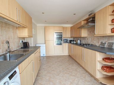 A kitchen with tiled floor wooden cabinets a built in oven and microwave and a washing machine at Wheal Kendall Mevagissey