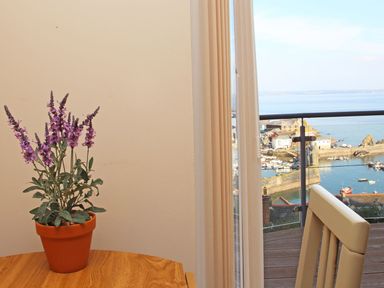 A potted purple flower on a wooden table next to a beige curtain and balcony with ocean view at Wheal Kendall in Mevagissey