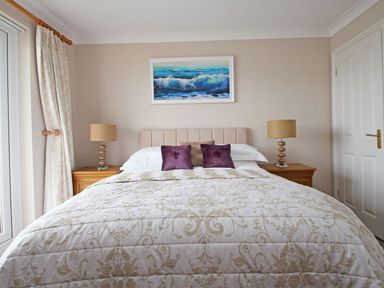 A bedroom with a bed with patterned quilt and pillows two bedside tables with lamps and a painting above the bed at Wheal Kendall in Mevagissey