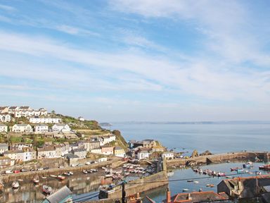 A coastal village with houses on a hillside and boats in a harbor at Wheal Kendall in Mevagissey