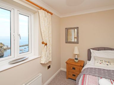 A bedroom corner with a bed bedside table lamp and window with a sea view at Wheal Kendall in Mevagissey