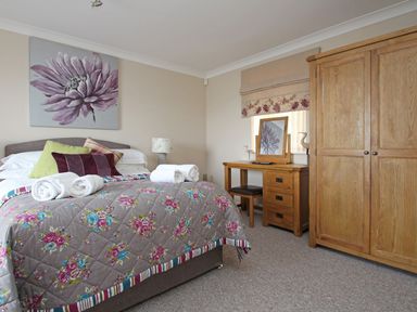 A bedroom with a bed and rolled towels a wooden dresser and wardrobe at Wheal Kendall in Mevagissey