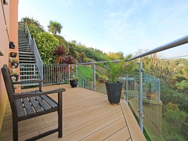 An outdoor balcony with a wooden bench potted plants glass railing and metal stairs leading to a garden at Wheal Kendall in Mevagissey