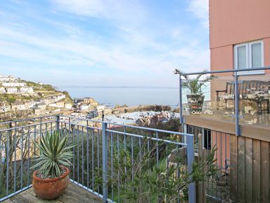 A balcony with metal railings and potted plants overlooking a coastal village and harbor at Wheal Kendall in Mevagissey
