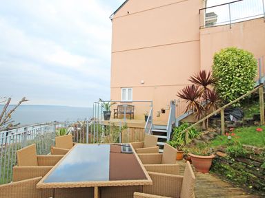An outdoor patio with a glass table and wicker chairs overlooking the sea at Wheal Kendall in Mevagissey