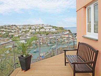 A balcony with a wooden bench and a potted plant overlooking a harbor and houses at Wheal Kendall in Mevagissey