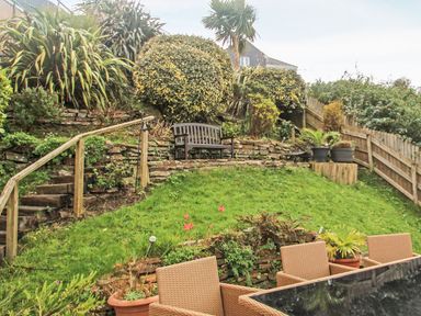 A garden with tiered stone walls wooden bench wicker chairs and plants at Wheal Kendall in Mevagissey