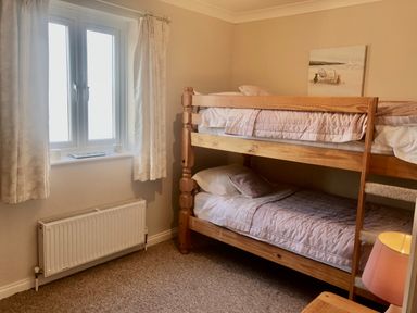 A bedroom with a wooden bunk bed a window with curtains and a radiator below at Wheal Kendall in Mevagissey