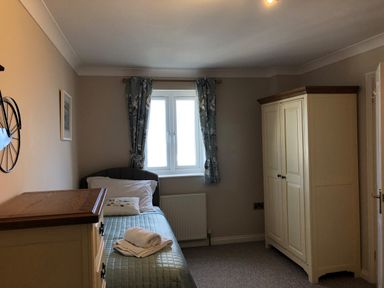 A bedroom with a single bed a chest of drawers a wardrobe and a window with curtains at Wheal Kendall in Mevagissey