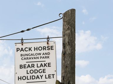 A wooden post with a hanging sign for Pack Horse Bungalow and Caravan Park and Bear Lake Lodge Holiday Let against a blue sky