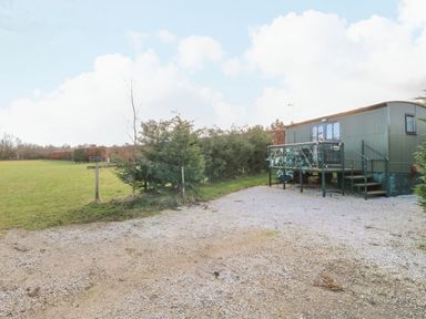 A small green shepherds hut with stairs and a railing on a gravel area next to grass and trees at Packhorse Shepherd's Hut in Alderwasley near Wirksworth