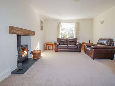 A living room with a fireplace two brown leather sofas and a window with curtains at Ilgram in St Newlyn East
