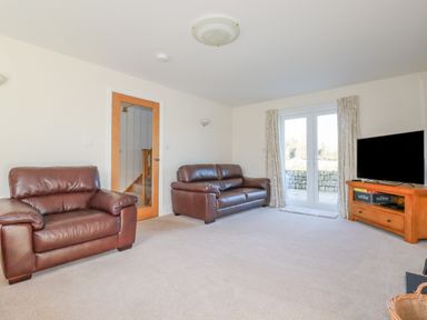 A living room with two brown leather sofas a wooden TV stand with a television and a glass door leading outside at Ilgram in St Newlyn East