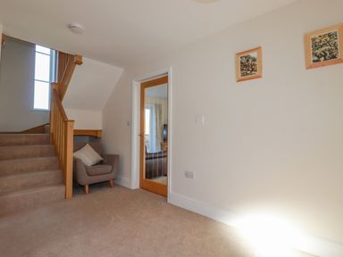 A hallway with stairs a gray armchair with a pillow and a wooden door with a glass panel at Ilgram in St Newlyn East