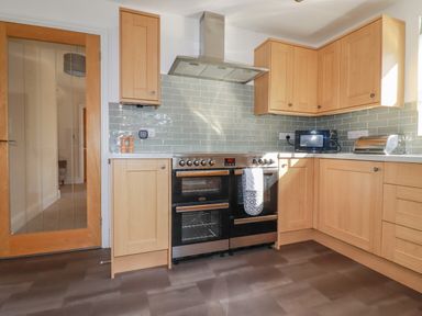A kitchen with wooden cabinets a stove a microwave a bread box and a glass door at Ilgram in St Newlyn East