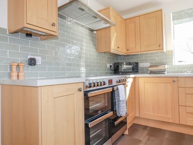 A kitchen with wooden cabinets a stove with oven a microwave and a bread bin at Ilgram in St Newlyn East