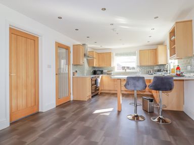 A kitchen with wooden cabinets, two grey bar stools, and two wooden doors at Ilgram in St Newlyn East