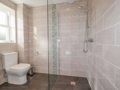 A bathroom with a toilet shower area glass partition and tiled walls at Ilgram in St Newlyn East