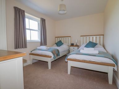 A bedroom with two single beds a nightstand between them and a window with curtains at Ilgram in St Newlyn East