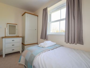 A bedroom with a bed towels on it a chest of drawers with a mirror and a wardrobe near a window with curtains at Ilgram in St Newlyn East