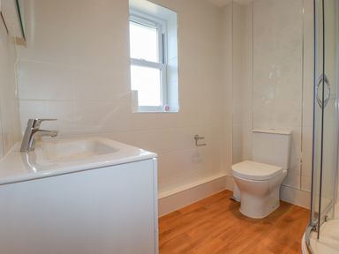 A bathroom with a sink, toilet, window, and shower with wooden floor at Ilgram in St Newlyn East