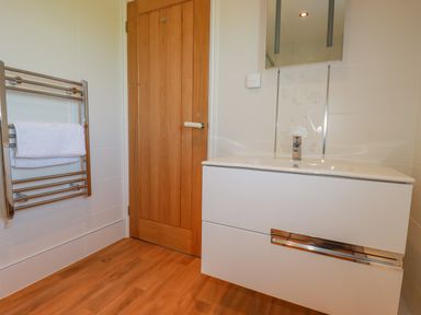 A bathroom with a wooden door a white sink cabinet a towel rack with a towel and wooden floor at Ilgram in St Newlyn East