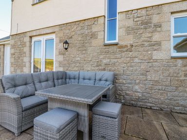An outdoor patio area with gray wicker corner sofa and table against a stone wall at Ilgram in St Newlyn East