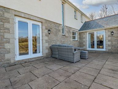 An outdoor patio area with stone walls glass doors and a wicker sofa set at Ilgram in St Newlyn East