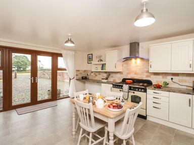 A kitchen with a wooden dining table set with food and drinks and white cabinets at Bramblewood Cottage in Crookdake near Bassenthwaite