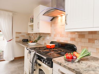 A kitchen with a stove a red pot a bowl of vegetables and white cabinets at Bramblewood Cottage in Crookdake near Bassenthwaite
