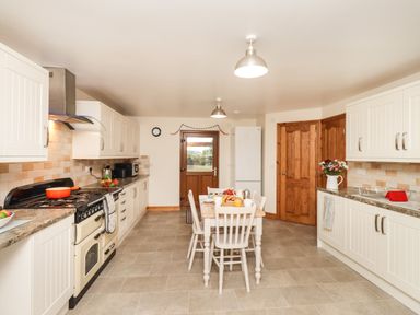 A kitchen with white cabinets a dining table with chairs and food items a stove and a refrigerator at Bramblewood Cottage in Crookdake near Bassenthwaite