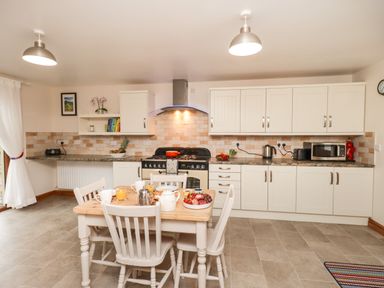 A kitchen with a wooden dining table and four chairs with food and drink on the table at Bramblewood Cottage in Crookdake near Bassenthwaite