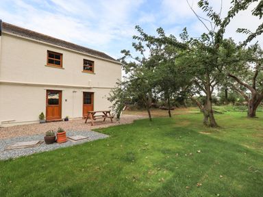 A garden with trees and grass next to a house with two wooden doors and a wooden picnic table at Bramblewood Cottage in Crookdake near Bassenthwaite