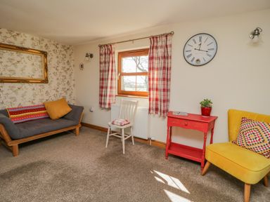 A living room with a gray sofa orange cushion yellow chair red table and white chair by a window at Bramblewood Cottage in Crookdake near Bassenthwaite