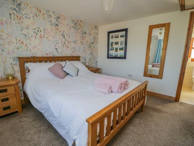 A bedroom with a wooden bed and floral wallpaper at Bramblewood Cottage in Crookdake near Bassenthwaite